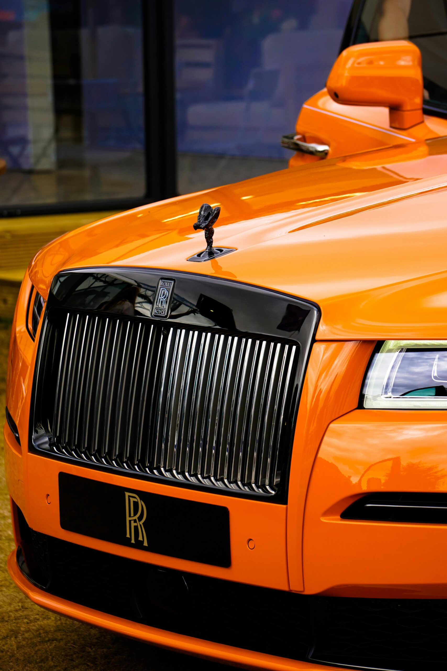 Close-up of a luxury orange car highlighting the iconic front grille emblem.